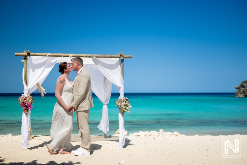 Couple shares a romantic kiss during their wedding ceremony at the stunning Daaibooi Beach in Curacao on a sunny day with a vibrant blue sky