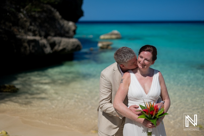 Couple celebrating their wedding at Daaibooi Beach in Curacao with stunning turquoise waters and rocky coastline in the background