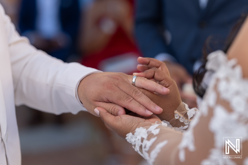 Couple exchanges wedding rings during ceremony at Avila Beach Hotel in Curacao surrounded by loved ones under bright blue sky
