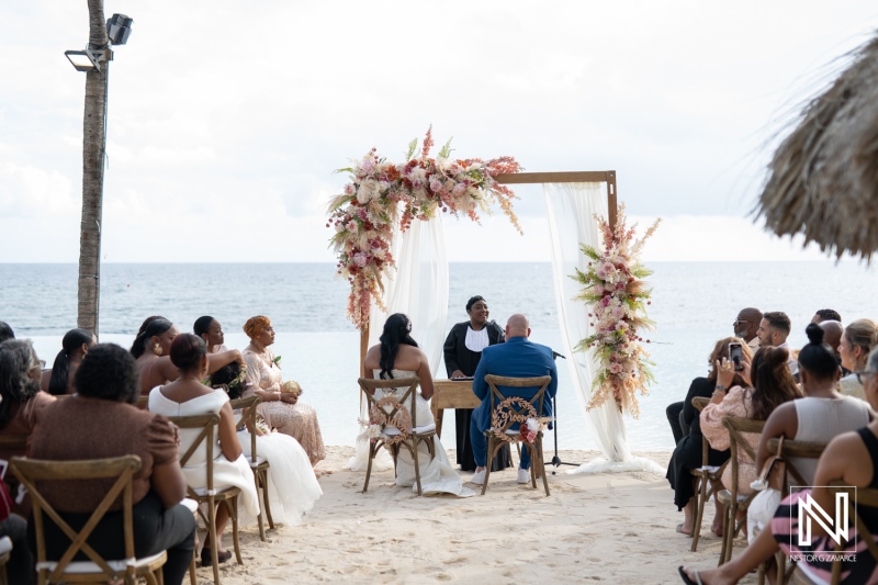 Elegant wedding ceremony by the beach at Renaissance Wind Creek Curacao Resort featuring floral arch and joyful guests