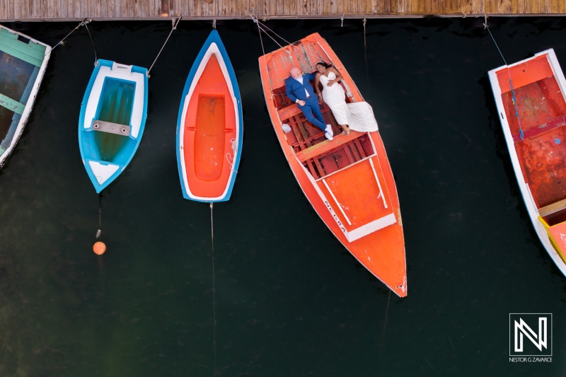Couple celebrates their wedding on an orange boat at Renaissance Wind Creek Curacao Resort surrounded by colorful vessels