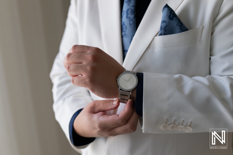 Groom adjusting his watch while dressed in a white suit during a wedding at Renaissance Wind Creek Curacao Resort