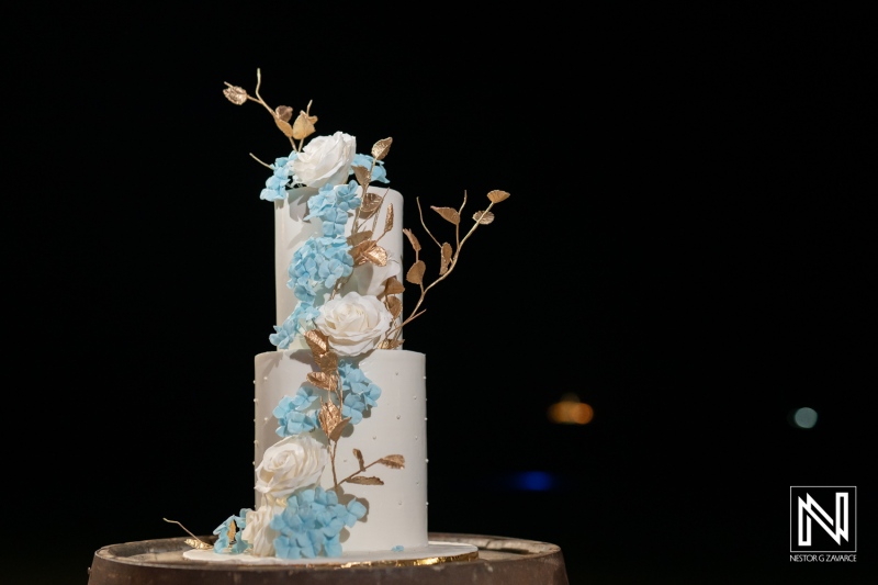 Elegant wedding cake adorned with blue flowers and golden accents at a celebration in Curacao