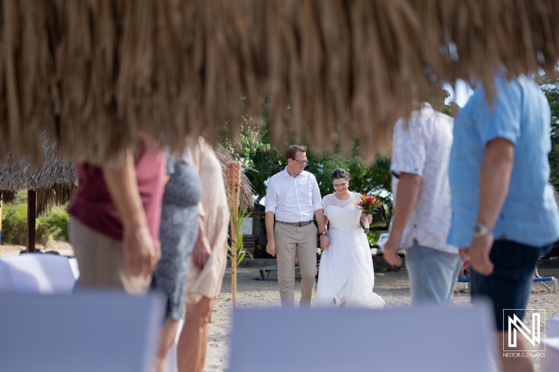 Couple walks hand in hand for their wedding ceremony on Daaibooi beach in Curacao surrounded by family and friends