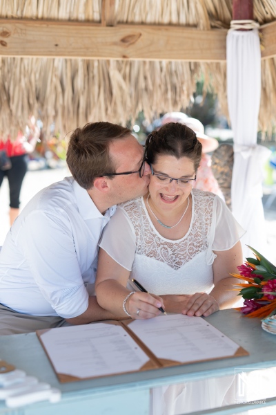 Couple joyfully signs wedding documents under a shelter in Daaibooi, Curacao while celebrating their love on a sunny day