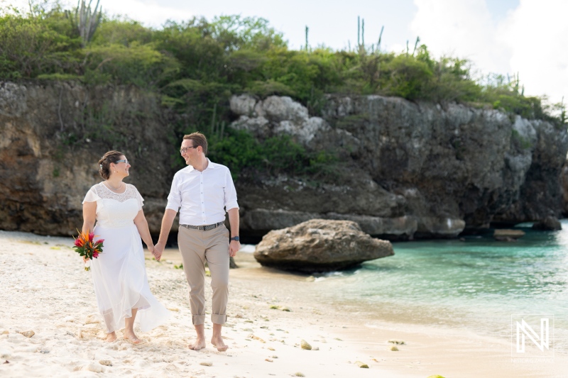 Beautiful wedding couple walking hand in hand on Daaibooi beach in Curacao with stunning natural scenery in the background