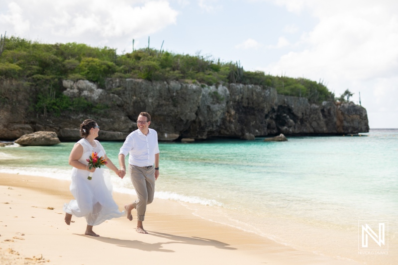 Couple joyfully running along the beach in Daaibooi, Curacao, celebrating their wedding day under a bright sunny sky