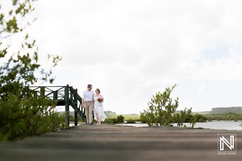 Couple walks hand in hand on a wooden pier in Daaibooi, Curacao during their wedding celebration against a scenic backdrop