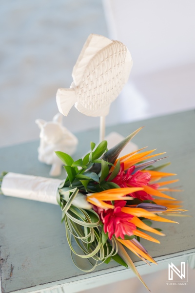 A Vibrant Tropical Wedding Bouquet With Orange and Red Flowers, Set Against a Pastel Background Featuring Decorative Fish and Elegant Craftsmanship