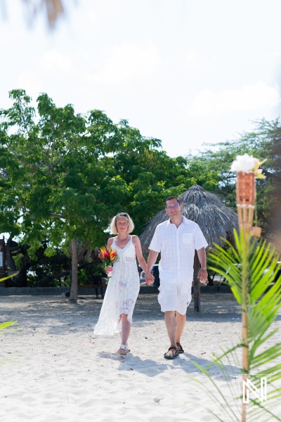 A Couple Strolls Hand in Hand Along a Sandy Beach, Surrounded by Lush Greenery and Tropical Decor, Enjoying a Warm Sunny Day