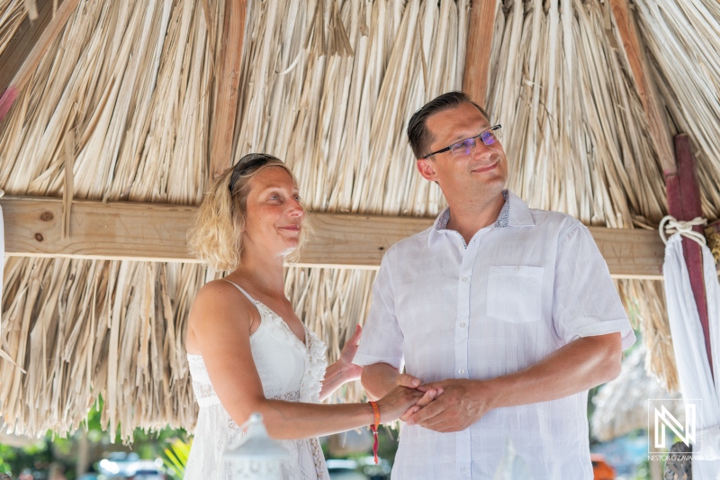 Couple Exchanging Vows Under a Thatched Roof at a Tropical Wedding Ceremony in a Lush Garden Setting During Daylight