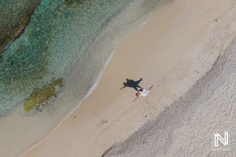 Aerial View of a Couple Enjoying a Romantic Moment on a Sandy Beach Surrounded by Clear Turquoise Waters During a Sunny Day