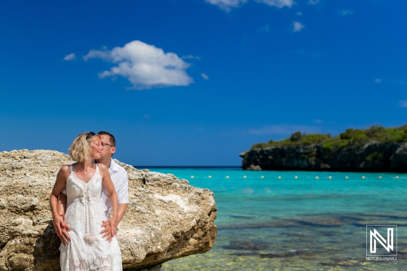 Couple Shares a Romantic Moment on a Rock by the Turquoise Waters of a Tropical Beach Under a Clear Blue Sky During a Sunny Day