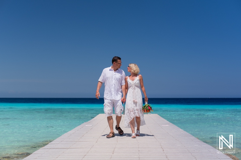 Couple Walks Hand in Hand Along a Wooden Pier by the Clear Turquoise Waters of a Tropical Paradise on a Sunny Day in a Romantic Setting