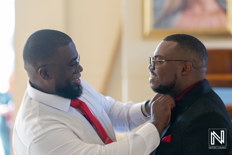 Groom adjusting best man's tie indoors at a Curacao wedding ceremony in a beautifully decorated venue