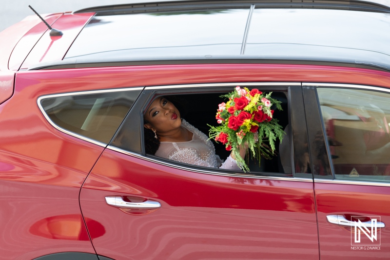 Beautiful bride in a red car holding a colorful bouquet, excited for her wedding in Curacao