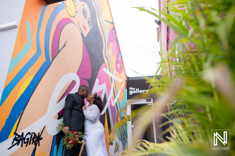 Couple shares a romantic kiss in front of vibrant mural during wedding celebration in Curacao