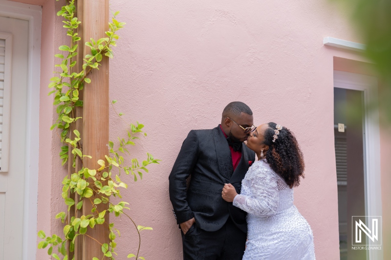Wedding couple shares a romantic kiss in Curacao against vibrant pink backdrop surrounded by greenery