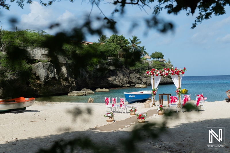 A Beach Wedding Setup on a Tropical Shore Featuring Floral Decorations, Chairs Arranged for Guests, and a Quaint Boat Under a Clear Blue Sky