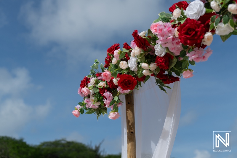 A Beautifully Decorated Floral Arch Featuring Red, Pink, and White Roses Against a Bright Sky at an Outdoor Event During the Day