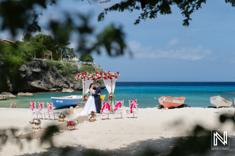 A Romantic Wedding Ceremony Takes Place on a Beautiful Beach With Decorated Floral Arch and Vibrant Chairs Under a Clear Blue Sky