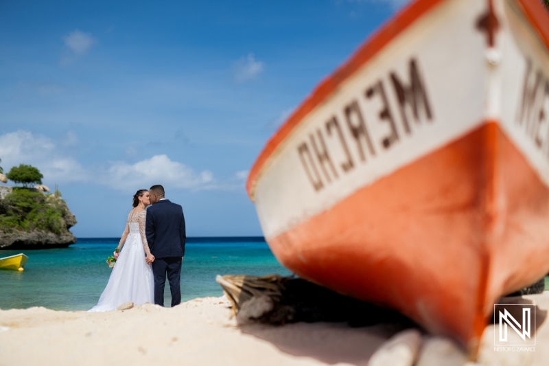 A Couple Embraces on a Beautiful Beach at Sunset, Surrounded by Tranquil Waters and a Vintage Boat in the Foreground, Capturing a Memorable Wedding Moment in Paradise