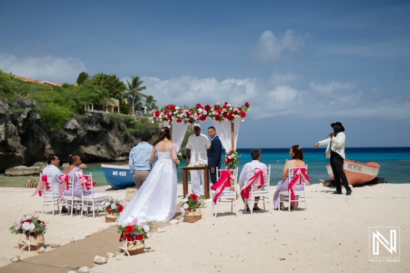 A Beautiful Beach Wedding Ceremony Takes Place Under a Floral Arch at a Tropical Location With Guests Dressed Elegantly on a Sunny Day