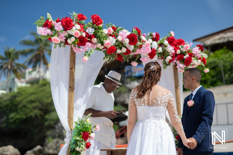 A Couple Exchanges Vows During a Beach Wedding Ceremony Adorned With Colorful Flowers in the Background, Capturing a Moment of Love Under a Clear Blue Sky