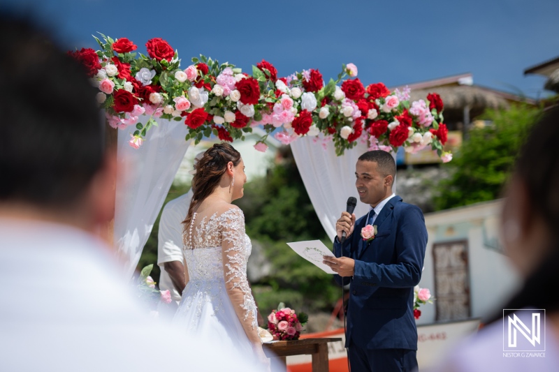 A Couple Exchanges Vows During a Beautiful Outdoor Wedding Ceremony Adorned With Floral Decorations in a Picturesque Setting on a Sunny Day