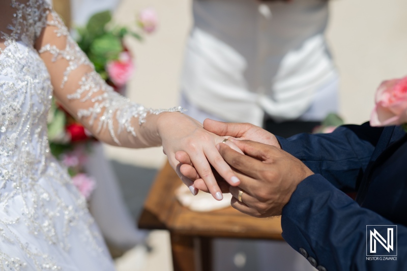 A Couple Exchanges Wedding Rings During an Outdoor Ceremony Surrounded by Floral Decorations, in Bright Sunlight, Capturing a Moment of Love and Commitment