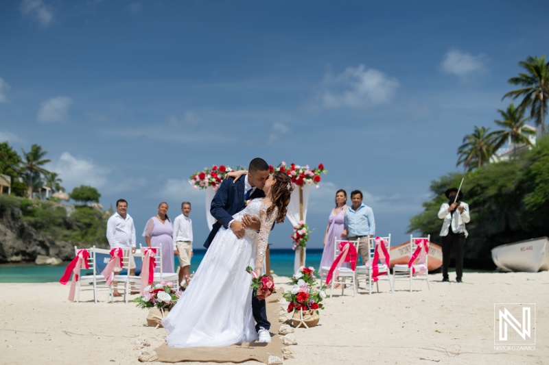 Couple Shares a Romantic Kiss During Their Beach Wedding Ceremony in a Tropical Paradise Under a Bright Sky and Surrounded by Friends and Family