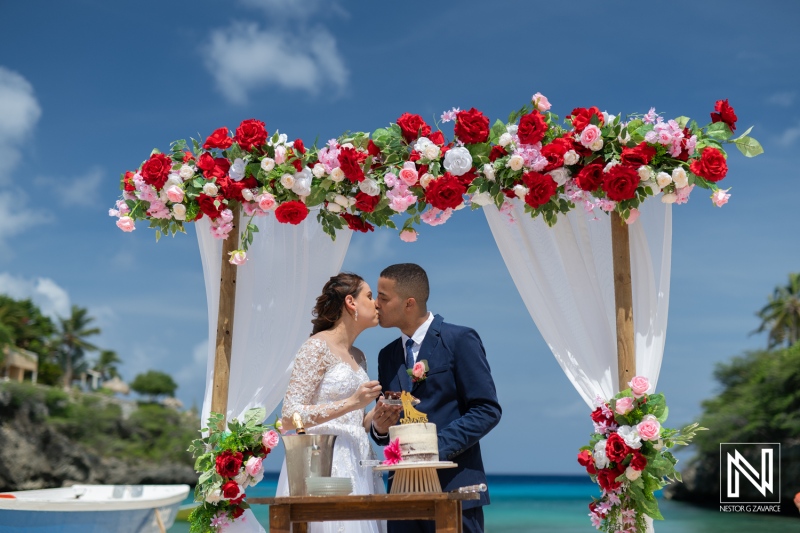 A Romantic Beachfront Wedding Ceremony at Sunset With a Beautifully Decorated Arch and a Couple Sharing a Kiss