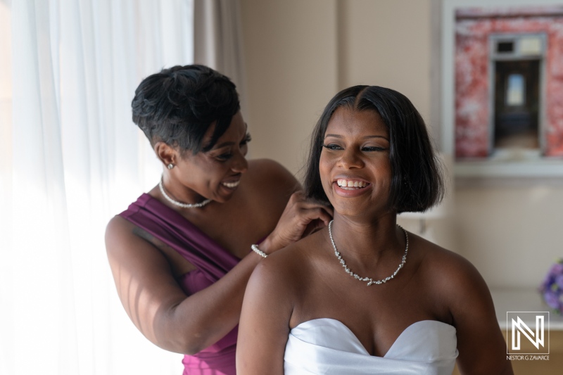 Two women share a joyful moment as one helps the other with her wedding dress in a bright and elegant bridal suite before the ceremony