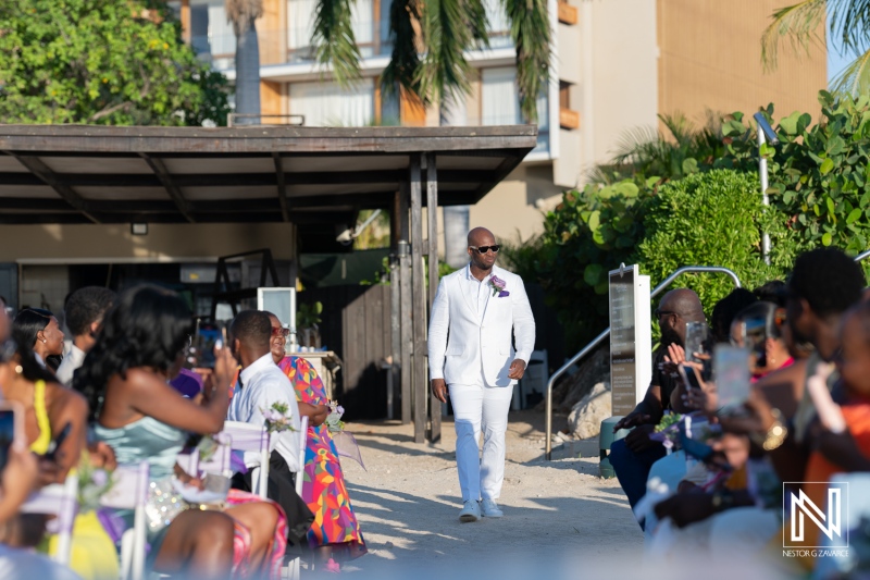 Groom walking down sandy aisle towards awaiting guests during sunset beach wedding ceremony in tropical setting