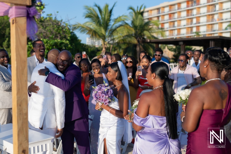 A joyful wedding ceremony in a tropical location with guests celebrating the union and an emotional embrace between the groom and best man during sunset