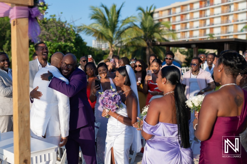 A joyful wedding ceremony in a tropical location with guests celebrating the union and an emotional embrace between the groom and best man during sunset