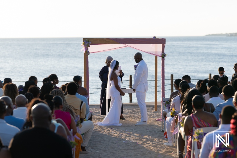 Outdoor beach wedding ceremony with guests seated on sand, couple exchanging vows at sunset near the ocean