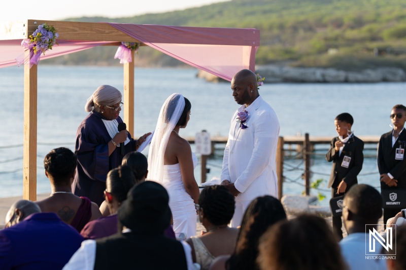 A beautiful beach wedding ceremony at sunset with an officiant, bride, groom, and guests in attendance near calm waters