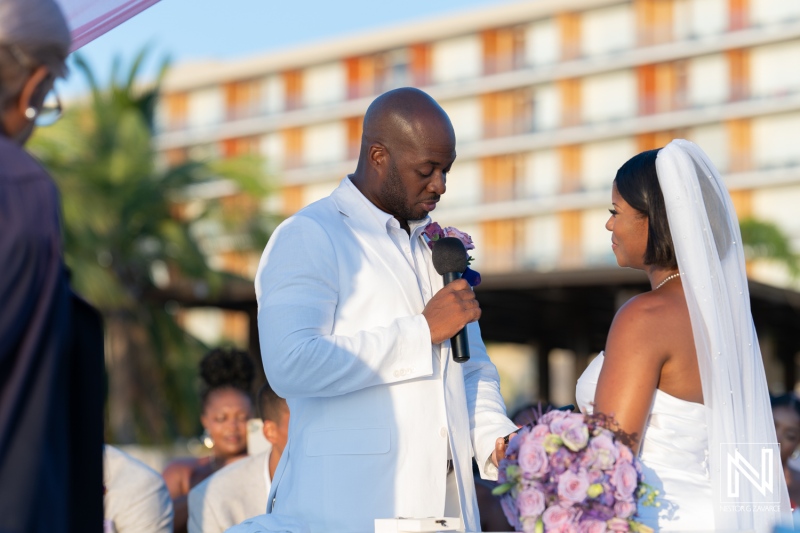 A couple exchanging vows during an outdoor wedding ceremony at a beach resort in the evening light with guests watching joyfully