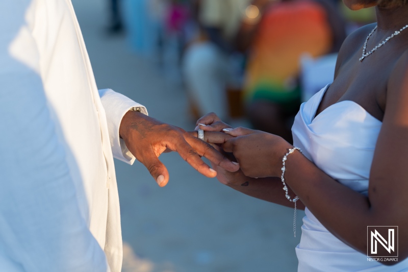 A couple exchanges wedding rings on a beautiful beach during a sunset ceremony surrounded by friends and family celebrating their love