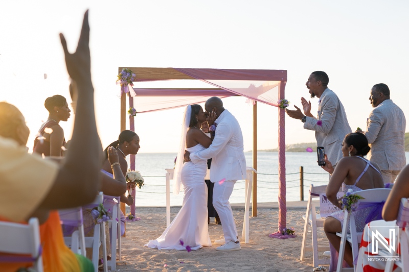 A beautiful beach wedding ceremony takes place at sunset with joyful guests celebrating the couple\'s love on a sandy shore