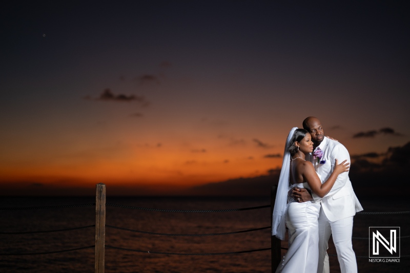 Couple embracing at sunset on tropical beach, celebrating wedding vows under the vibrant sky with colorful sunset hues