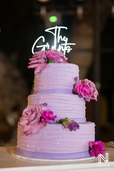 A beautiful three-tier lavender wedding cake adorned with fresh flowers and a custom topper celebrating the bride and groom at an elegant reception venue