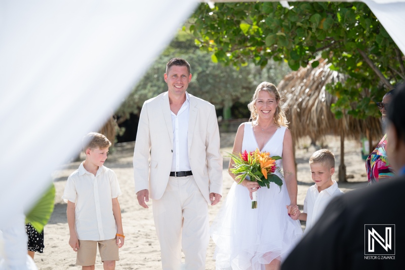 Couple walks on Daaibooi Beach in Curacao for a wedding ceremony at The Kontiki Curacao Beach Resort with children