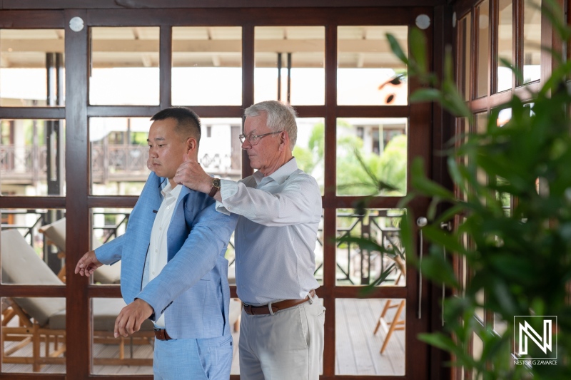 Groom prepares for wedding ceremony at Kokomo Beach in Curacao with assistance from a family member