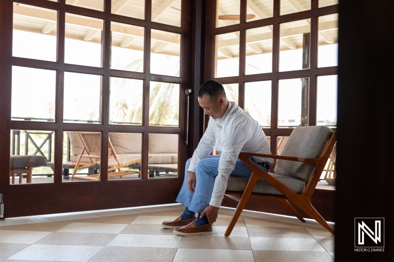 Groom prepares for wedding day at Kokomo Beach in Curacao with a moment of quiet reflection and careful attire adjustment