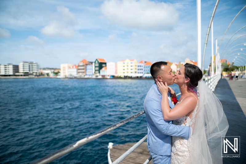 Couple shares a romantic kiss at Kokomo Beach during their wedding ceremony in Curacao, surrounded by scenic ocean views and vibrant architecture