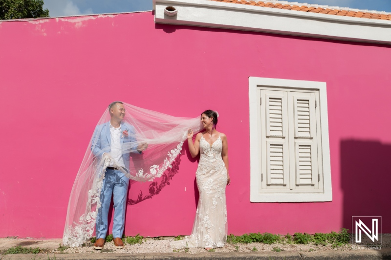 Couple joyfully celebrates their wedding at Kokomo Beach in Curacao amidst vibrant pink walls and beautiful surroundings