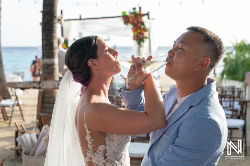 Couple celebrates their wedding at Kokomo Beach Curacao with drinks and joy while the sun sets over the ocean landscape