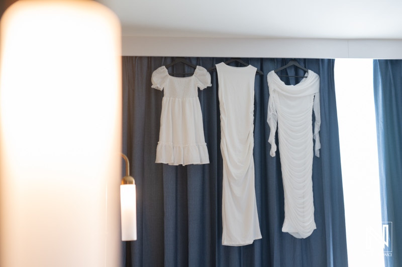 Three elegant white dresses hanging on a curtain in a well-lit room, creating a stylish display for fashion enthusiasts at a clothing boutique